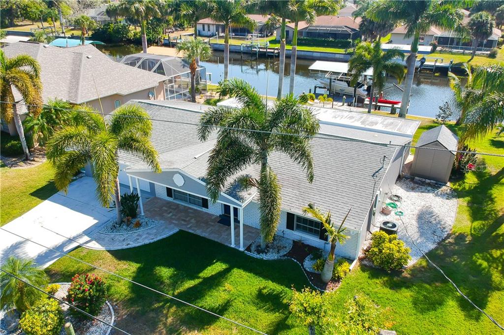 An aerial view of a single-story house with a gray roof, palm trees, and canal — 18289 WOLBRETTE CIRCLE, PORT CHARLOTTE, FL