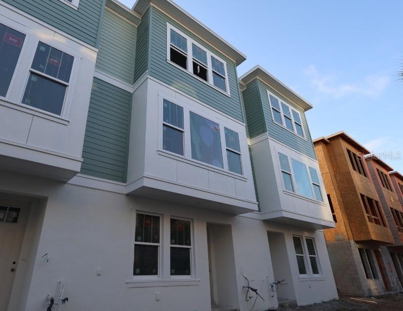 A low-angle exterior view of a multi-story townhouse with teal siding and white stucco — 466 31ST WAY N UNIT 9, ST PETERSBURG, FL