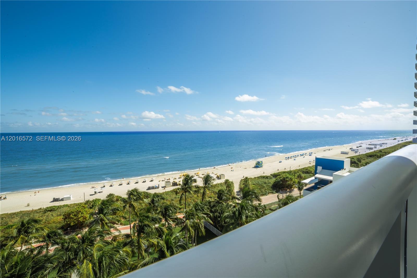 A high-angle view shows a sandy beach, ocean, and palm trees from a balcony — 6301 Collins Ave # 1102, Miami Beach FL 33141, MIAMI BEACH, FL