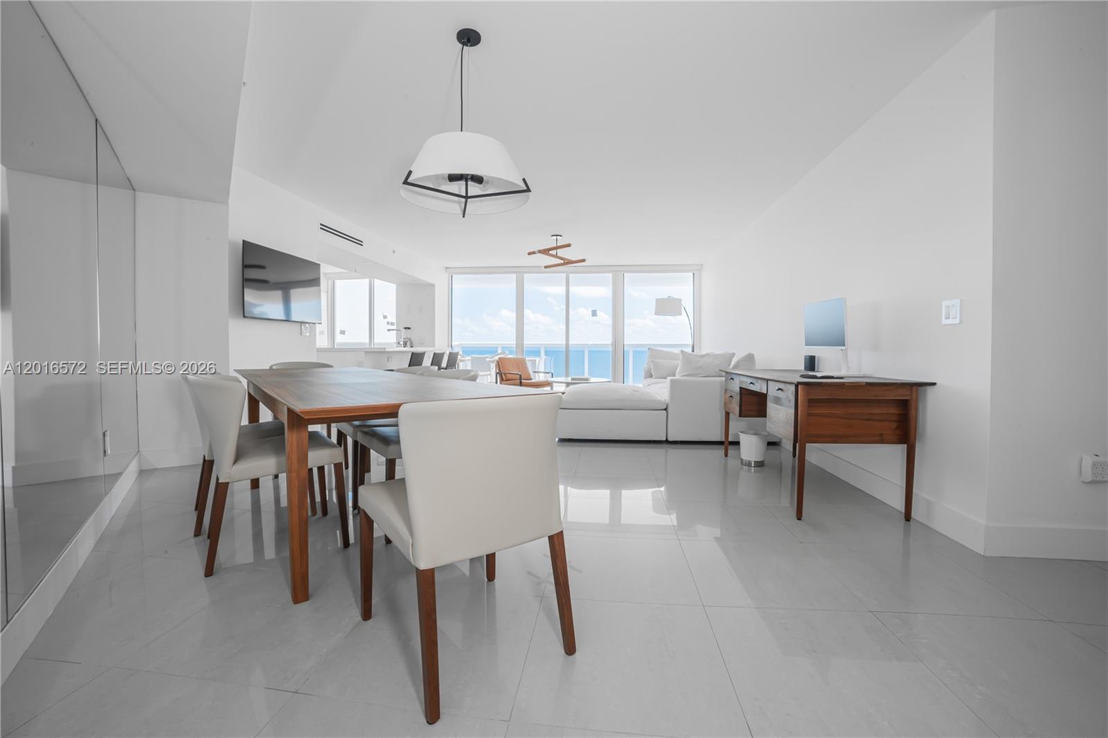 A bright, open-concept living and dining area features white tile floors and ocean views — 6301 Collins Ave # 1102, Miami Beach FL 33141, MIAMI BEACH, FL