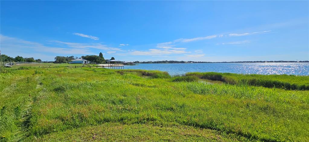 A grassy shoreline leads to a lake with a wooden pier and distant houses — US HIGHWAY 630 W, FROSTPROOF, FL