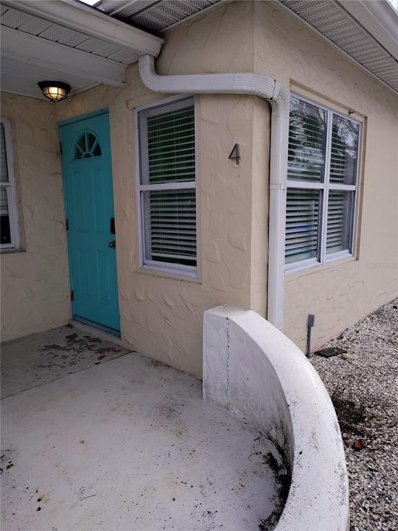 A light-colored exterior wall features a turquoise door, two windows, and a curved concrete wall — 115 145TH AVENUE E UNIT 4, MADEIRA BEACH, FL