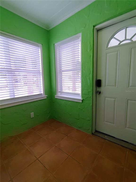 An entryway with bright green textured walls, tile flooring, two windows with blinds, and a door — 115 145TH AVENUE E UNIT 4, MADEIRA BEACH, FL