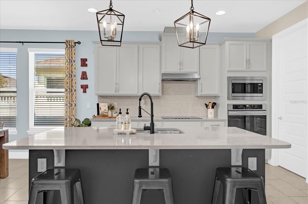 A modern kitchen features a dark gray island, light gray cabinets, and two pendant lights — 224 VENETIAN PALMS BOULEVARD, NEW SMYRNA BEACH, FL