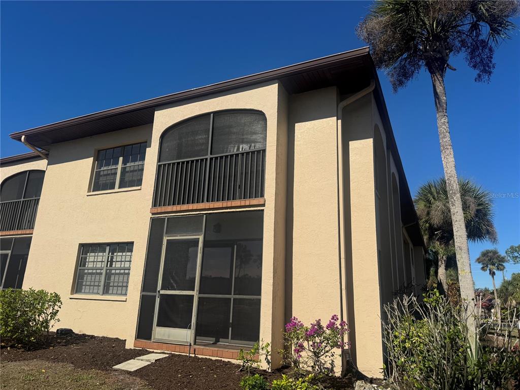 The exterior of a two-story tan stucco building features screened balconies and a palm tree — 23465 HARBORVIEW ROAD UNIT 201, PUNTA GORDA, FL