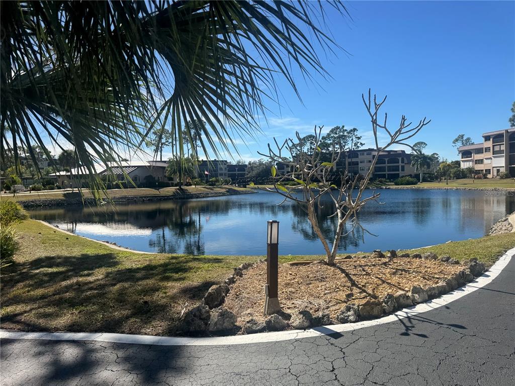 A view of a pond surrounded by apartment buildings and landscaping under a clear sky — 23465 HARBORVIEW ROAD UNIT 201, PUNTA GORDA, FL