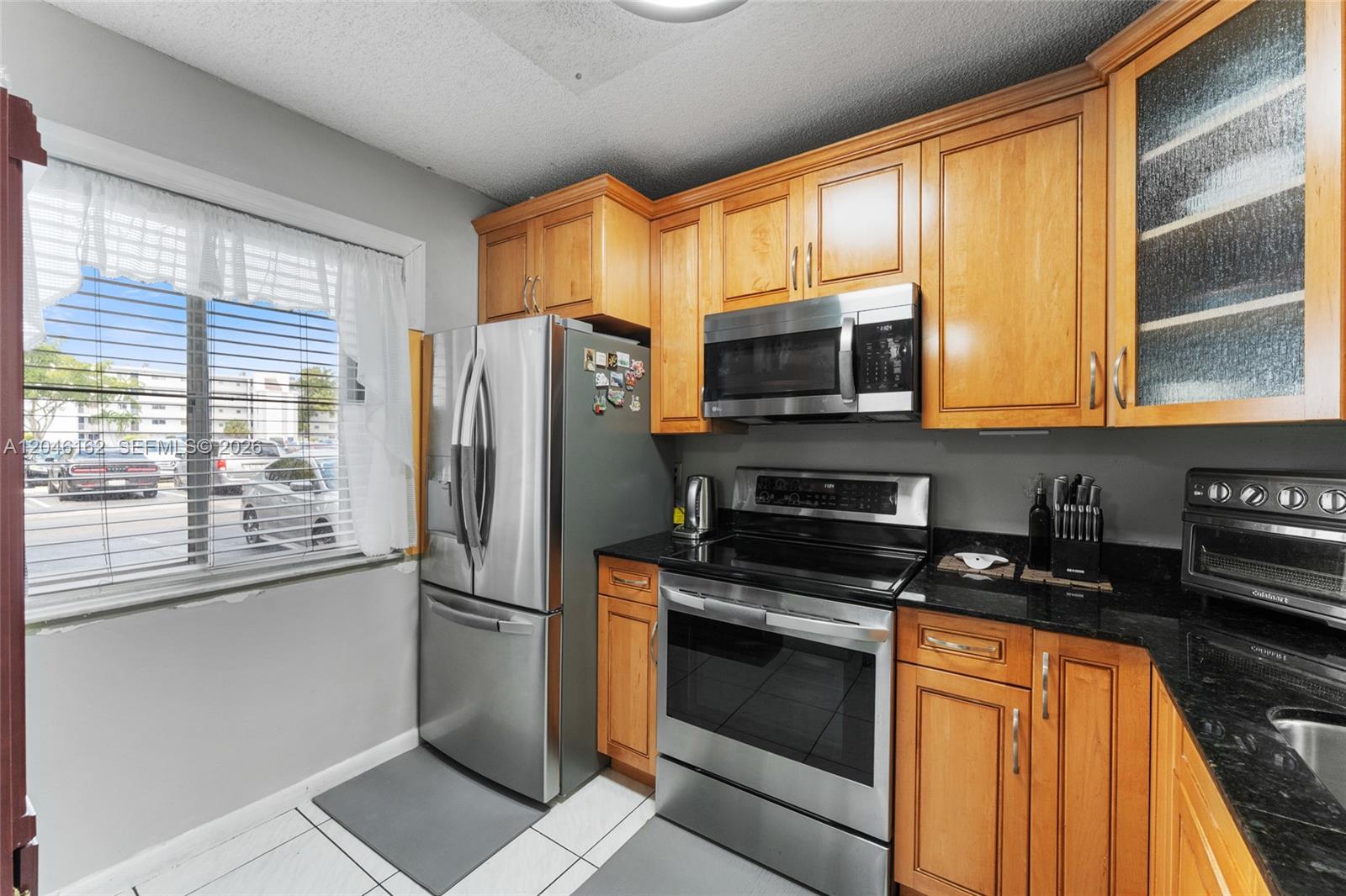 A kitchen features wood cabinets, stainless steel appliances, and black countertops next to a window — 8550 N Sherman Cir # 108, Miramar FL 33025, MIRAMAR, FL