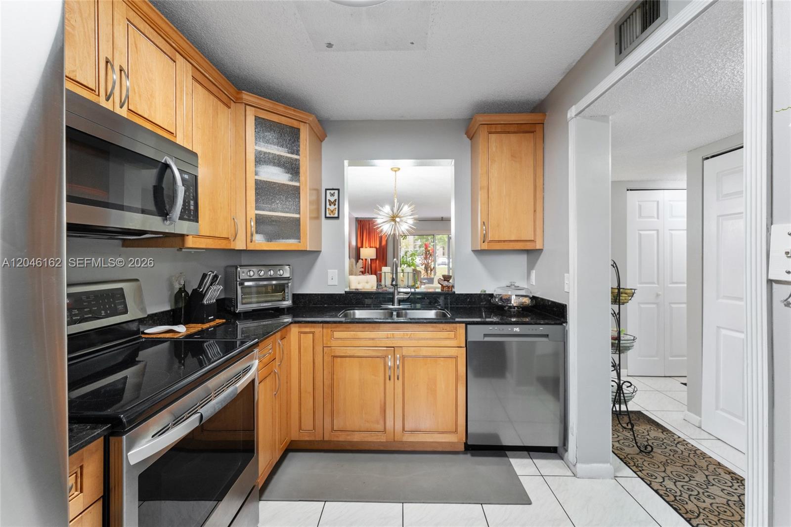 A kitchen features light wood cabinets, black countertops, stainless steel appliances, and a pass-through window — 8550 N Sherman Cir # 108, Miramar FL 33025, MIRAMAR, FL