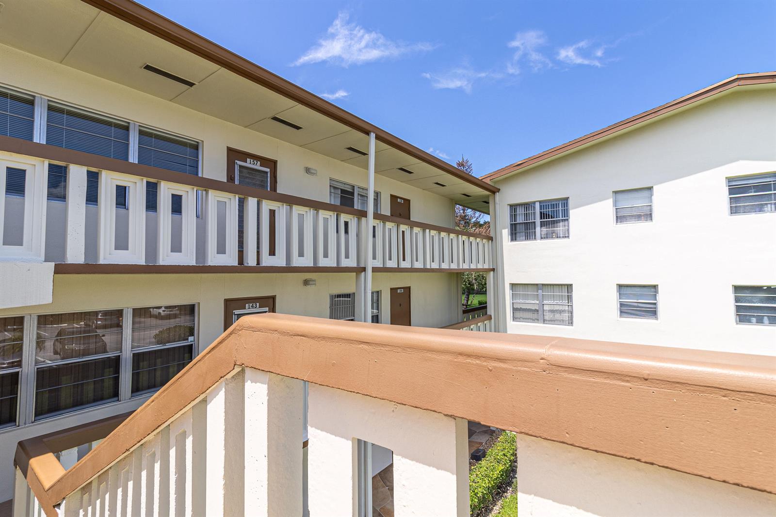 An exterior view of a multi-story apartment building with open walkways and brown railings — 158 Mansfield D Drive, Boca Raton FL 33434, BOCA RATON, FL