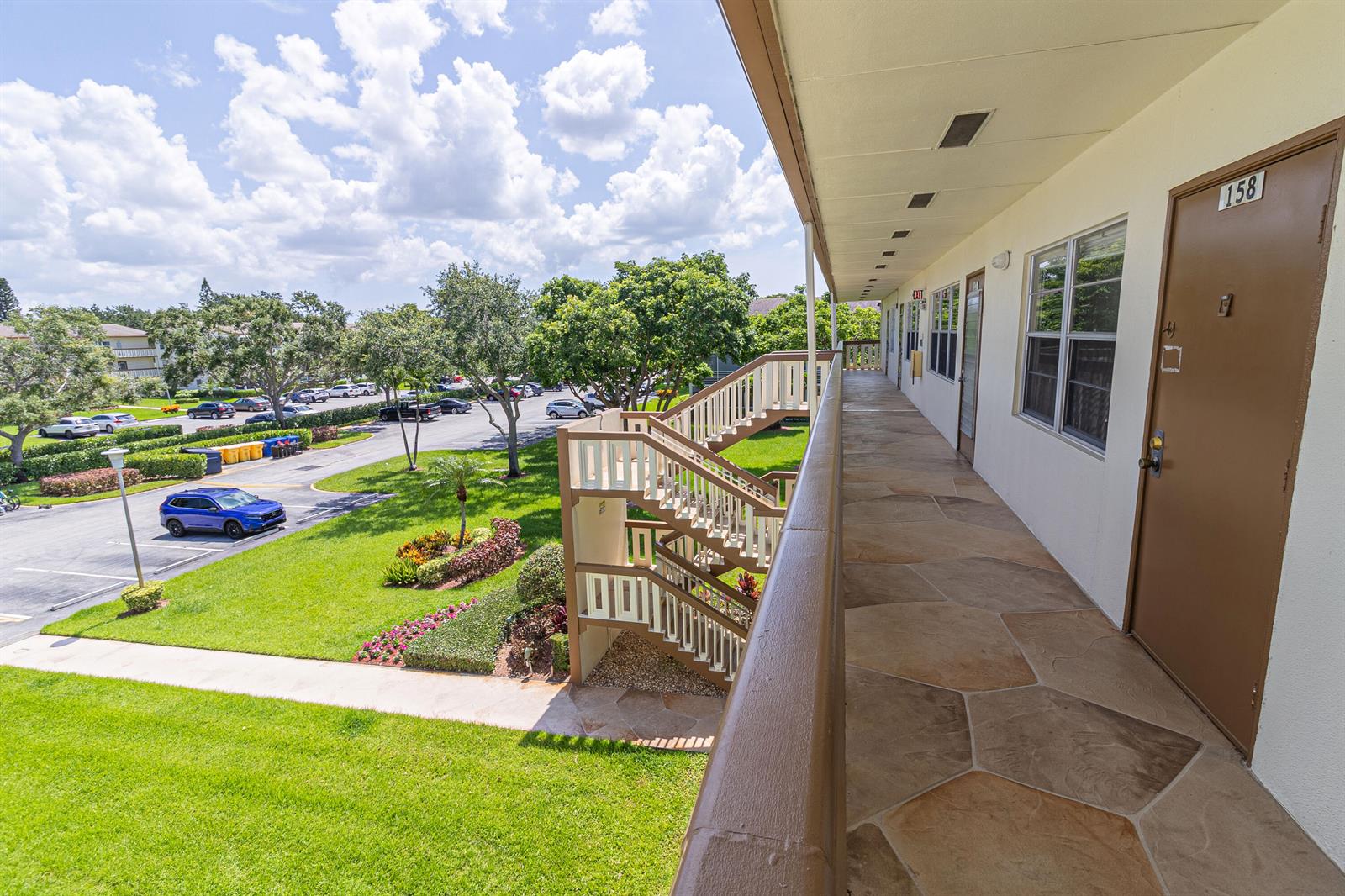 An outdoor walkway with stone flooring leads to apartment doors next to a wooden staircase — 158 Mansfield D Drive, Boca Raton FL 33434, BOCA RATON, FL