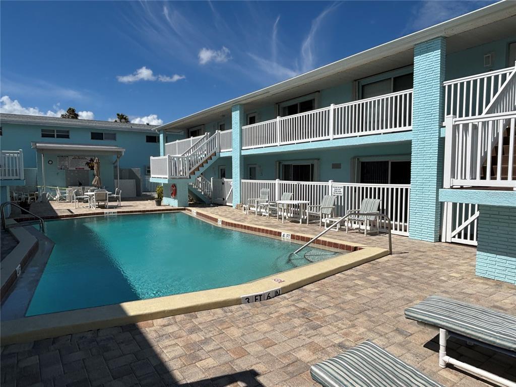 An outdoor swimming pool sits in front of a two-story light blue apartment building — 180 FLAGLER LANE UNIT 26, COCOA BEACH, FL