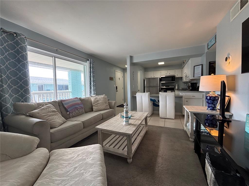 A living room with a sofa, coffee table, and an open kitchen with white cabinets — 180 FLAGLER LANE UNIT 26, COCOA BEACH, FL