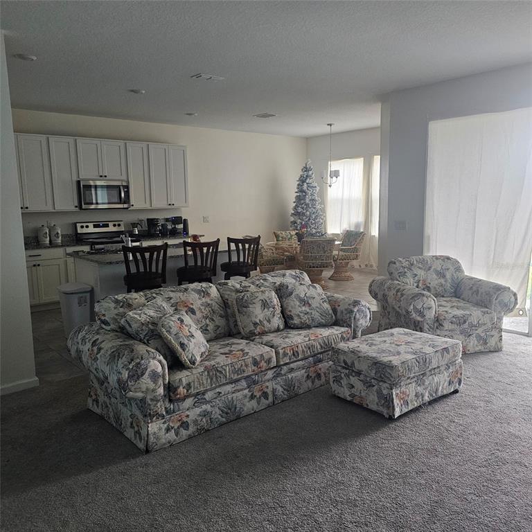 An open-concept living room features floral furniture, carpeted floors, and a kitchen with white cabinetry — 299 BOTTLE BRUSH DRIVE, HAINES CITY, FL