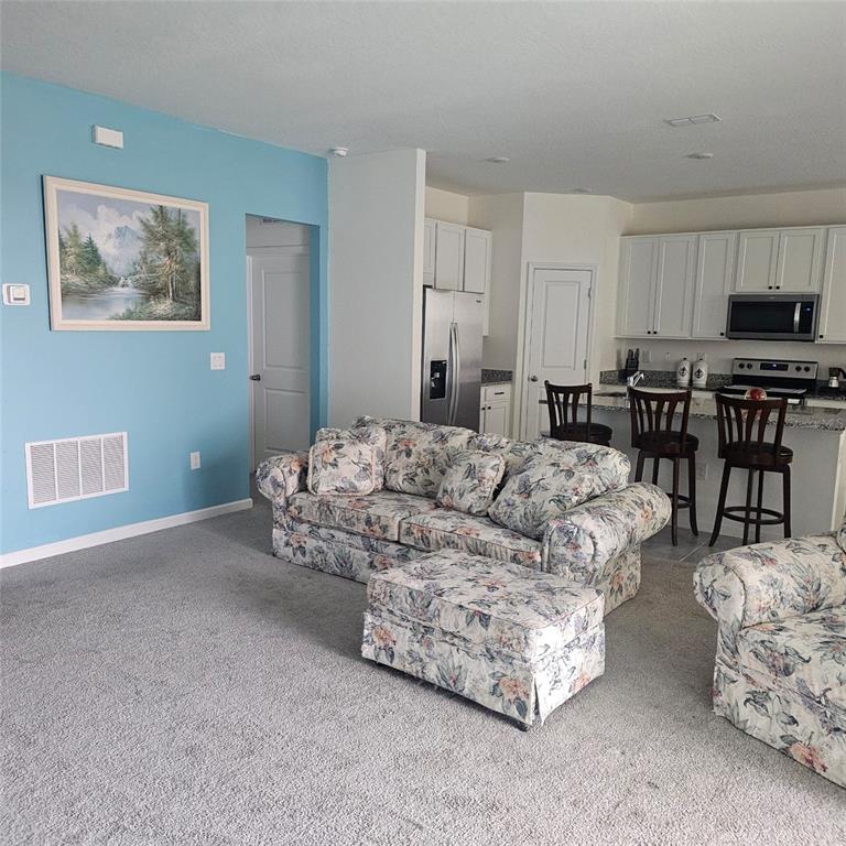 A living room with floral furniture and gray carpet opens into a kitchen with white cabinets — 299 BOTTLE BRUSH DRIVE, HAINES CITY, FL