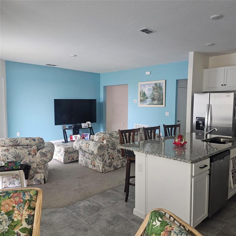 A living room with blue walls and floral furniture opens to a kitchen with granite countertops — 299 BOTTLE BRUSH DRIVE, HAINES CITY, FL