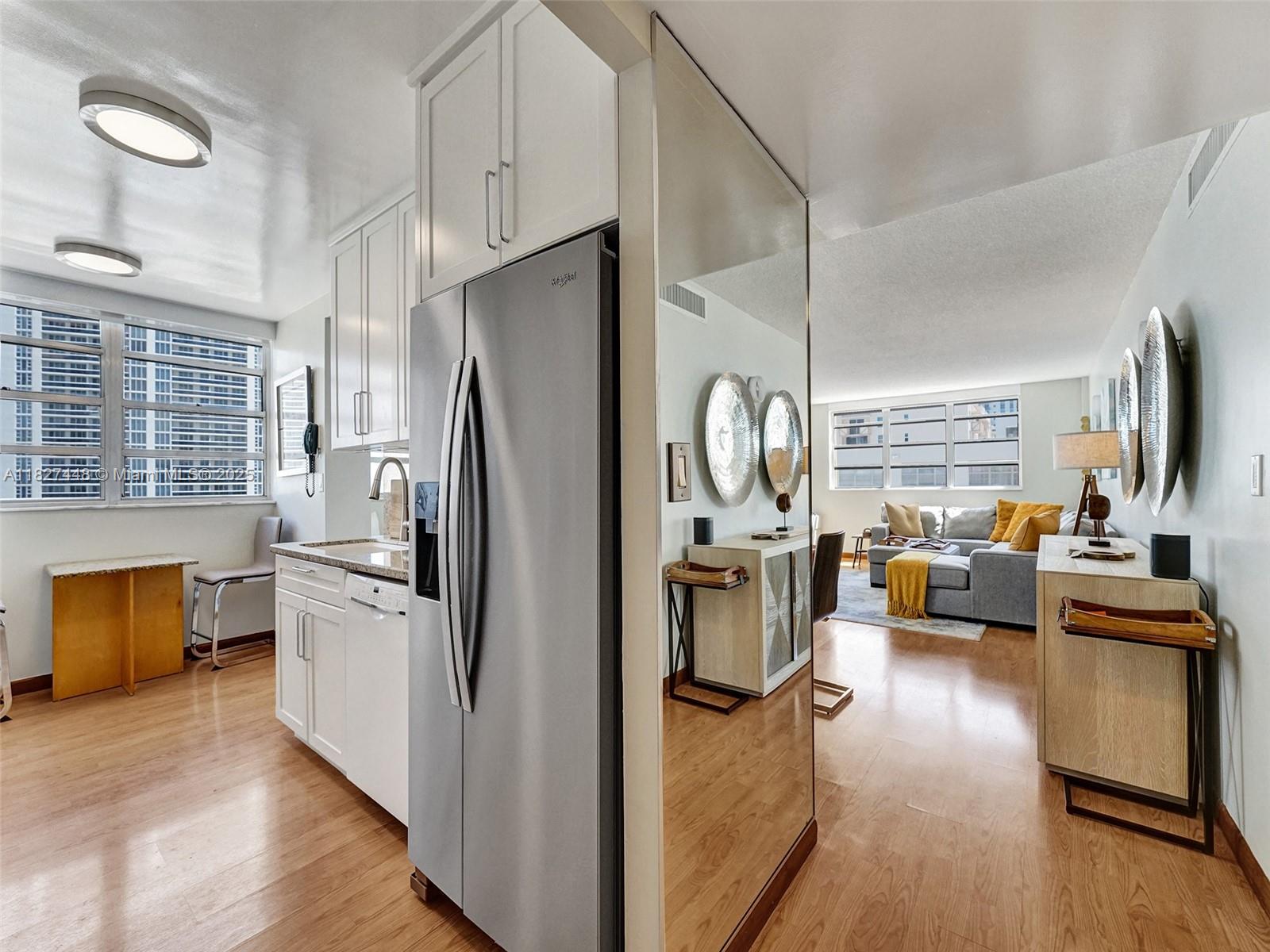 A kitchen with white cabinets and stainless steel appliances opens into a living room area — 1833 S Ocean Dr # 1702, Hallandale Beach FL 33009, HALLANDALE BEACH, FL