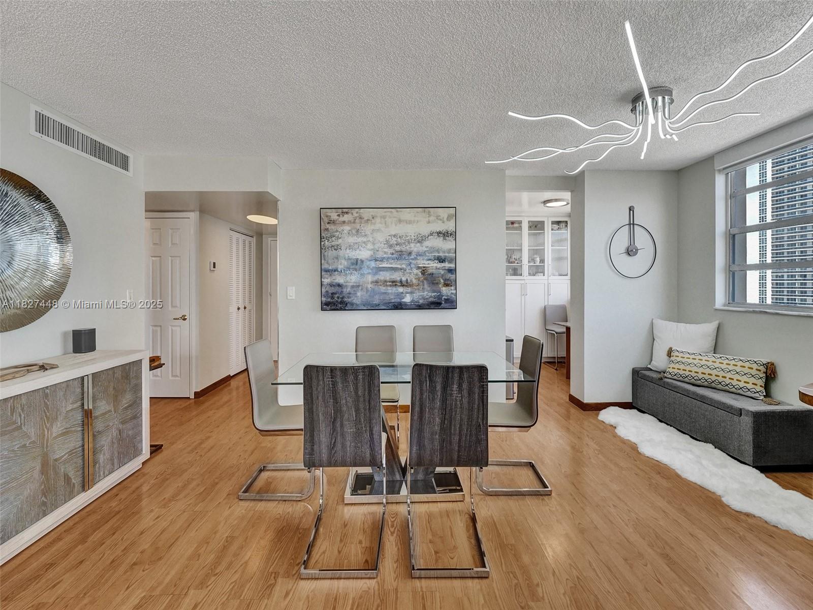 A dining room features a glass table, modern chairs, a unique light fixture, and wood flooring — 1833 S Ocean Dr # 1702, Hallandale Beach FL 33009, HALLANDALE BEACH, FL