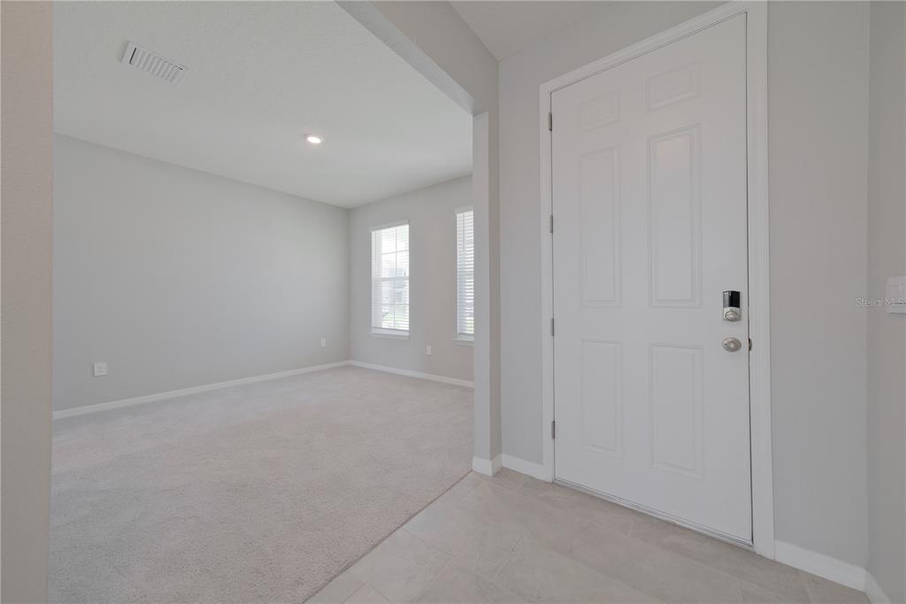 An entryway with light tile flooring leads into a carpeted room with two windows — 5748 WOODLAND SAGE DRIVE, SARASOTA, FL
