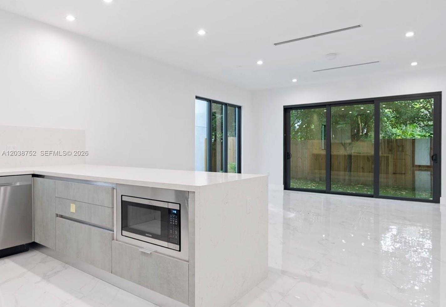 A modern kitchen features white countertops, light gray cabinetry, and sliding glass doors to a yard — 3374 Perry Frow Dr # B, Miami FL 33133, MIAMI, FL
