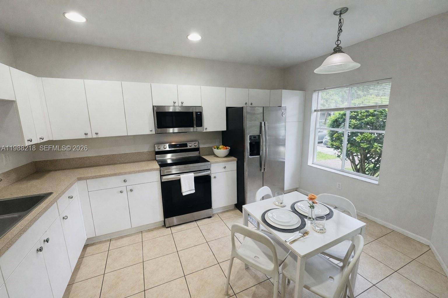 A kitchen features white cabinets, stainless steel appliances, tan countertops, and a small dining area — 8225 SW 29th St # 102, Miramar FL 33025, MIRAMAR, FL