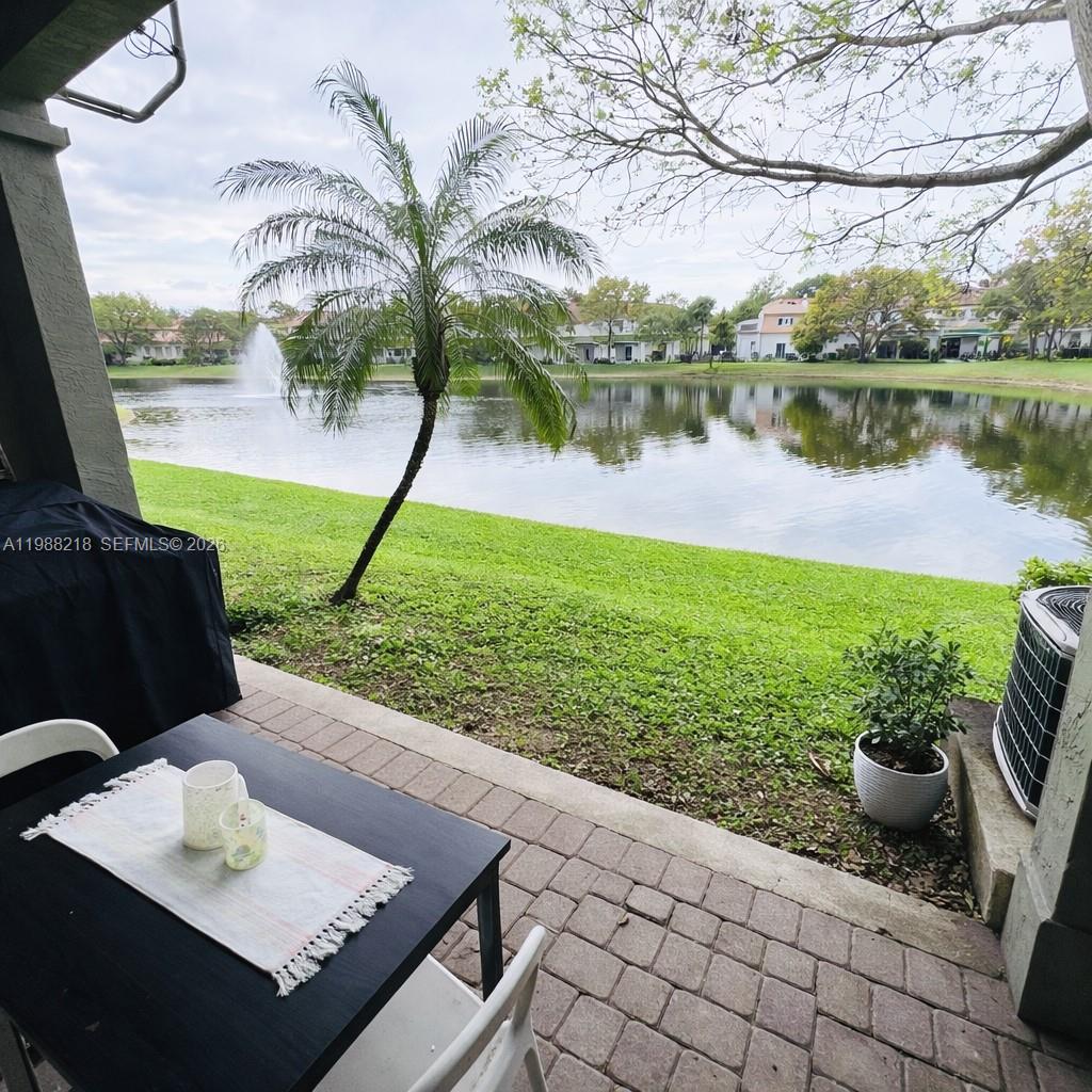 A patio with a table overlooks a grassy lawn, a pond, and a fountain — 8225 SW 29th St # 102, Miramar FL 33025, MIRAMAR, FL