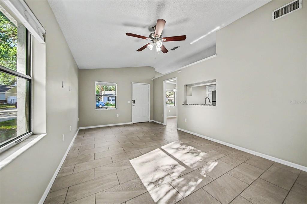A living room with light-colored tile flooring, a ceiling fan, and a pass-through kitchen window — 2710 LORRAINE DRIVE, LEESBURG, FL