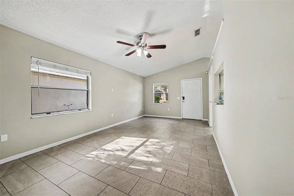 An empty living room features light-colored walls, tile flooring, a ceiling fan, and two windows — 2710 LORRAINE DRIVE, LEESBURG, FL
