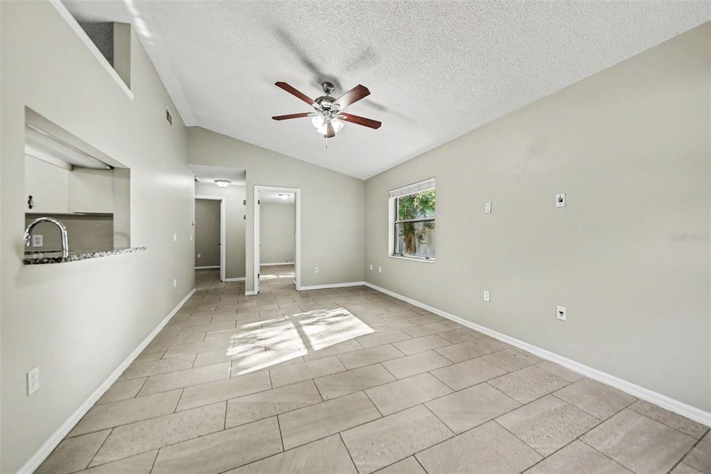 An empty living room with vaulted ceilings, a ceiling fan, and light-colored tile flooring — 2710 LORRAINE DRIVE, LEESBURG, FL