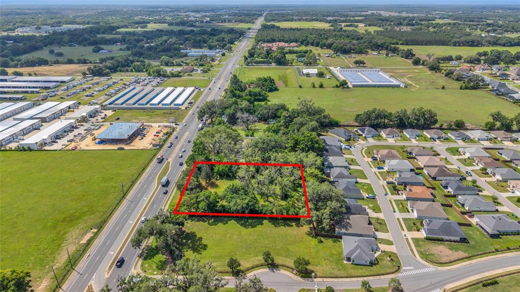 An aerial view shows a rectangular, tree-filled vacant lot outlined in red near a highway — 11338 N US HIGHWAY 301, OXFORD, FL