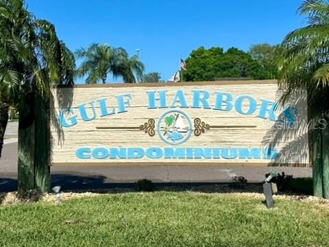 A sign for Gulf Harbors Condominiums stands outdoors surrounded by palm trees and grass — 5207 TURQUOISE LANE UNIT 202, NEW PORT RICHEY, FL
