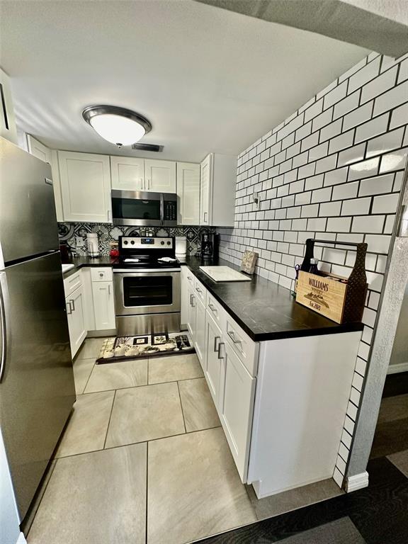 A galley kitchen features white cabinets, stainless steel appliances, dark countertops, and white subway tile walls — 5207 TURQUOISE LANE UNIT 202, NEW PORT RICHEY, FL