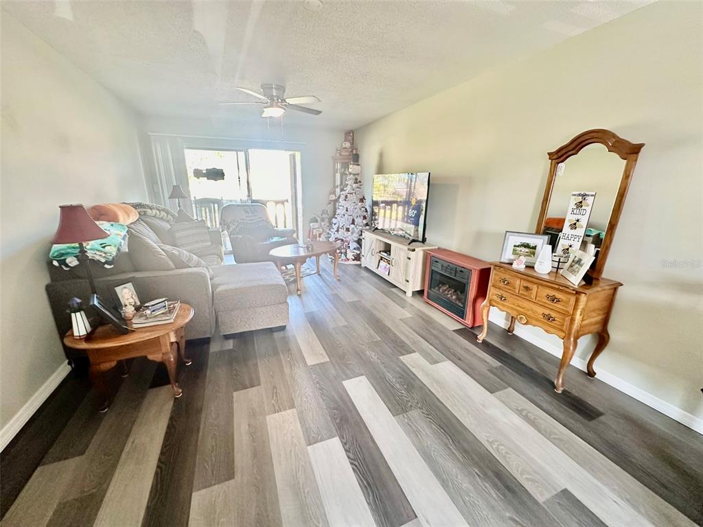 A living room features wood-look flooring, a sectional sofa, a television console, and a vanity — 5207 TURQUOISE LANE UNIT 202, NEW PORT RICHEY, FL