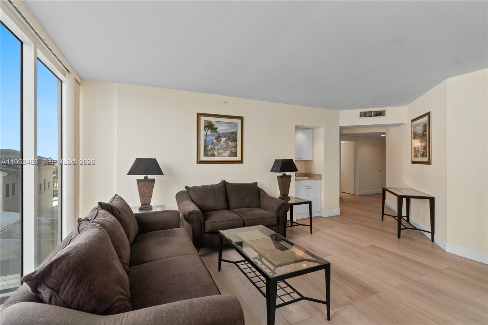 A living room features brown sofas, a glass coffee table, and light wood flooring — 4775 Collins Ave # 507, Miami Beach FL 33140, MIAMI BEACH, FL