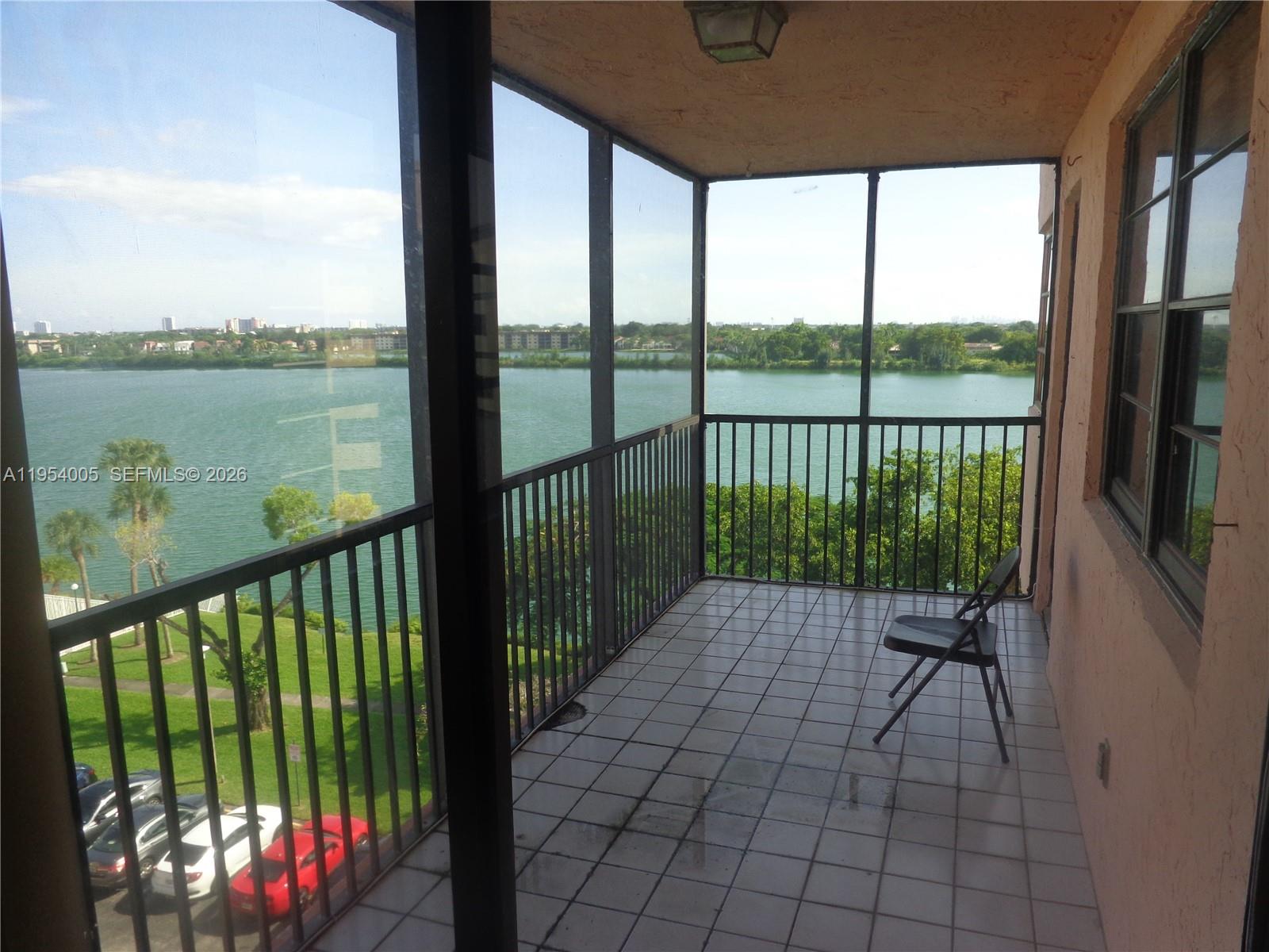 A screened-in balcony with tile flooring overlooks a lake and parking area — 20850 San Simeon Way # 5, Miami FL 33179, MIAMI, FL