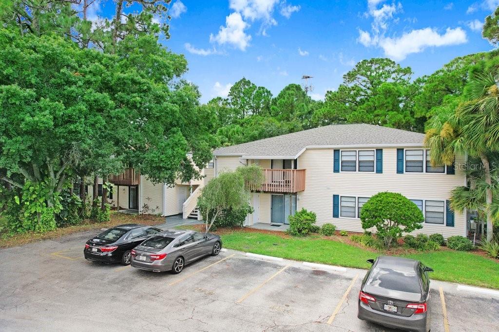 A two-story apartment building with beige siding, a parking lot, and surrounding trees — 134 SYCAMORE LANE UNIT F, OLDSMAR, FL