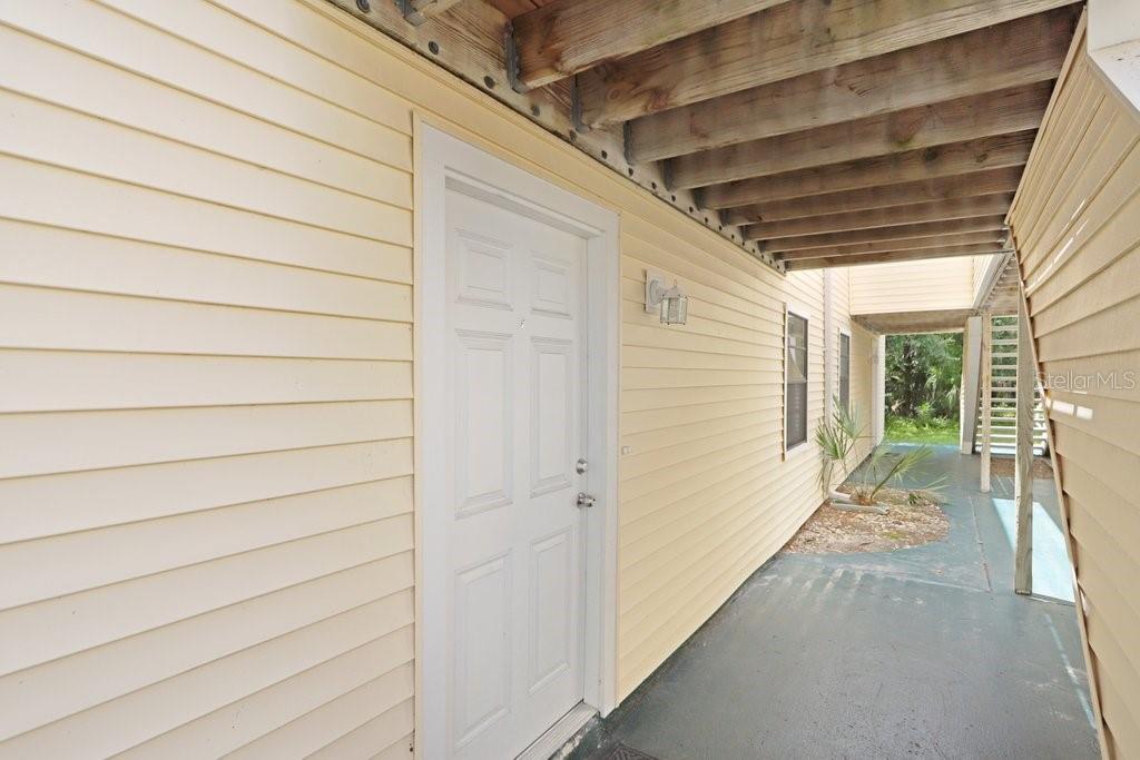 A white door is set into the light yellow vinyl siding of an exterior building walkway — 134 SYCAMORE LANE UNIT F, OLDSMAR, FL