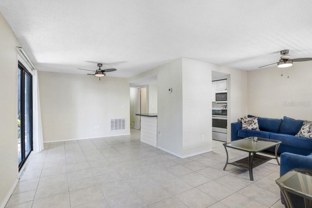 An open-concept living room features light tile flooring, a blue sofa, and a kitchen pass-through — 134 SYCAMORE LANE UNIT F, OLDSMAR, FL