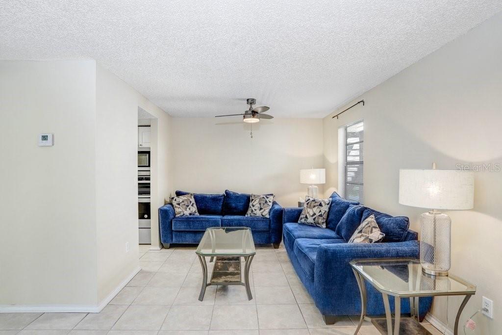 A living room features two blue sofas, a glass coffee table, and light tile flooring — 134 SYCAMORE LANE UNIT F, OLDSMAR, FL