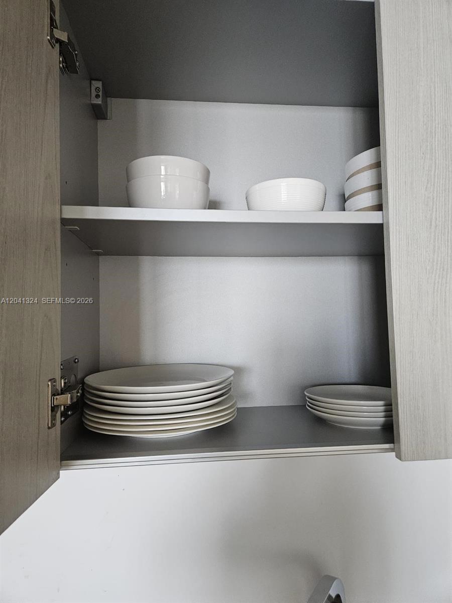 An open kitchen cabinet contains stacks of white plates and bowls on two shelves — 4111 S Ocean Dr # 1204, Hollywood FL 33019, HOLLYWOOD, FL