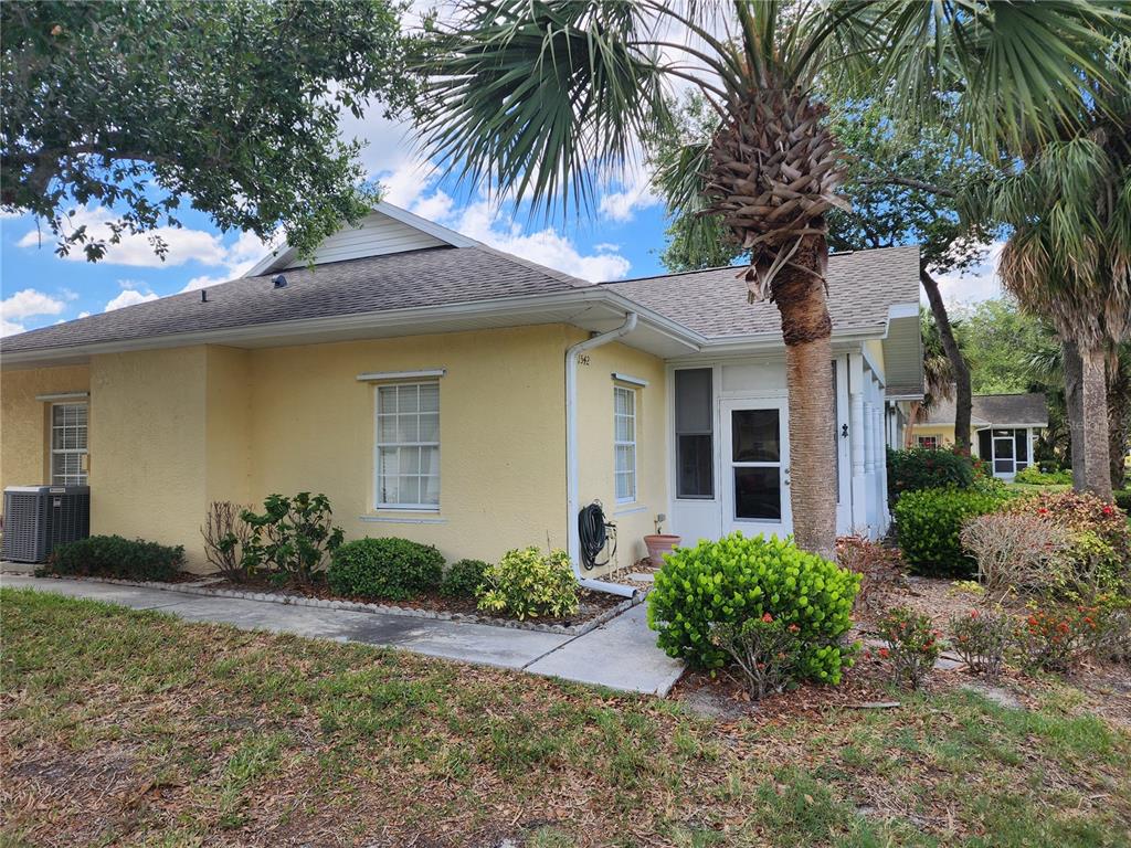 A yellow stucco house with a shingled roof, a front porch, and a palm tree — 1542 RED OAK LANE, PORT CHARLOTTE, FL