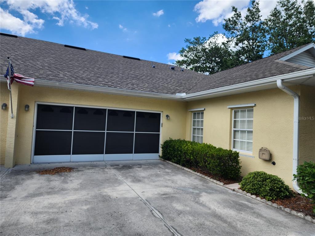 A yellow house exterior features a screened garage door, a concrete driveway, and two windows — 1542 RED OAK LANE, PORT CHARLOTTE, FL