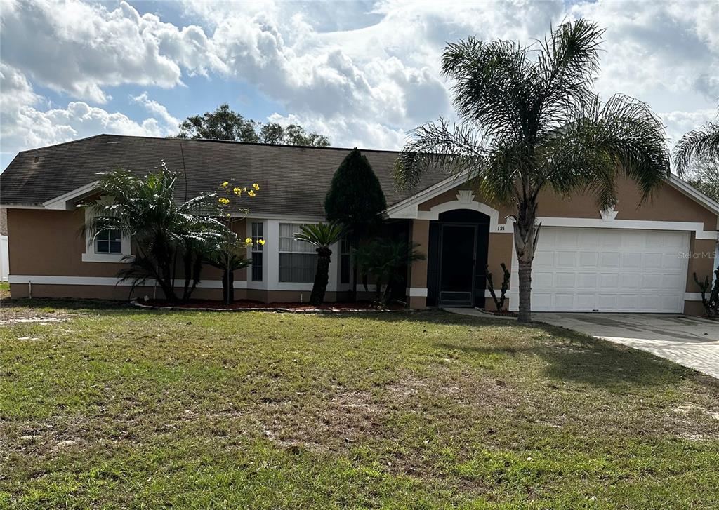 A single-story house with a tan exterior, a white garage door, and a palm tree — 121 LOMA BONITA DRIVE, DAVENPORT, FL