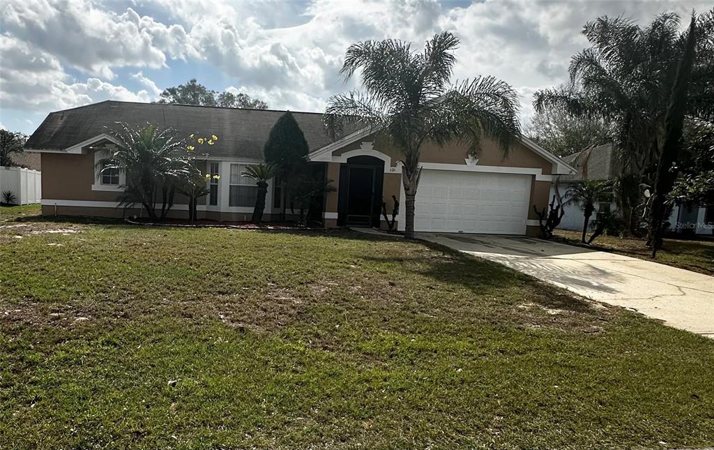 A single-story house with a white garage door, a palm tree, and a grassy lawn — 121 LOMA BONITA DRIVE, DAVENPORT, FL
