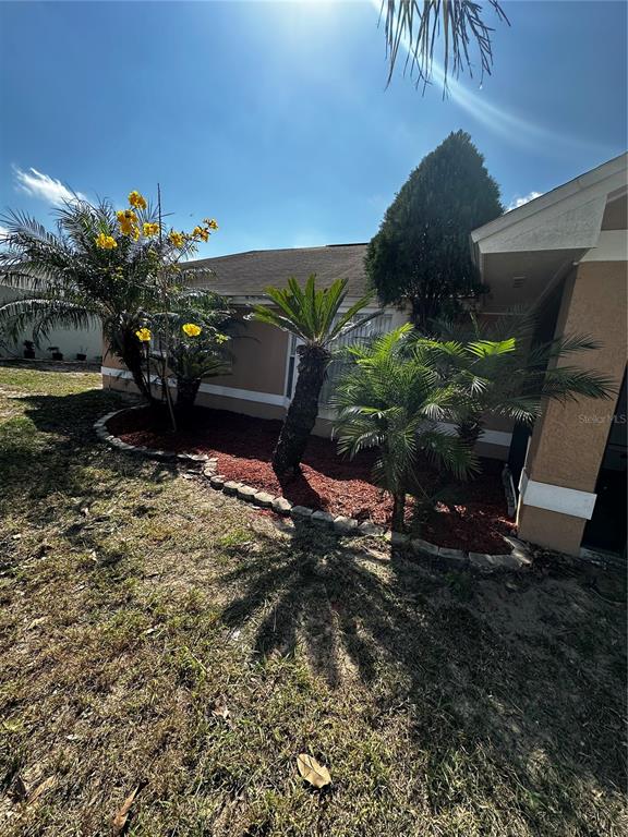 A tan house exterior features a landscaped garden bed with palm trees and yellow flowers — 121 LOMA BONITA DRIVE, DAVENPORT, FL