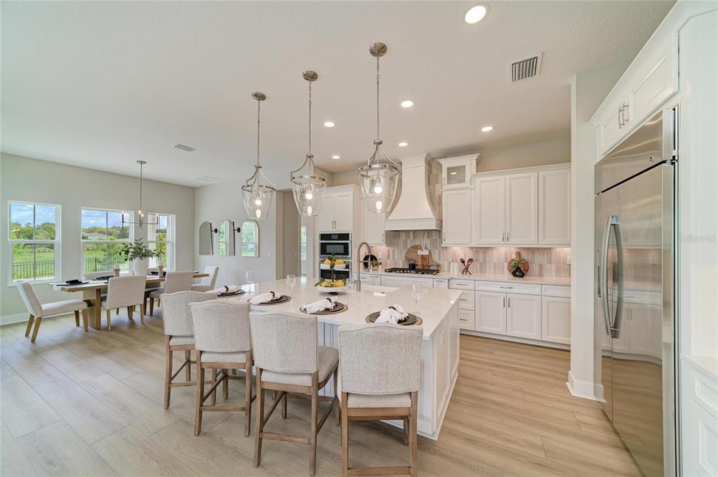 A bright kitchen features white cabinetry, a large center island with seating, and wood-look flooring — 1132 BUCK CREEK COURT, BRANDON, FL