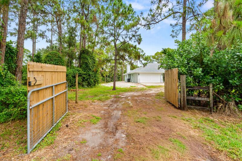 A dirt driveway leads through an open wooden gate toward a house with a garage — 12689 N 68th St Street N, FL 33412, FL