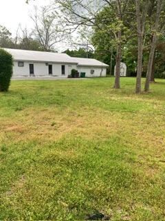 A white, single-story building sits behind a large, grassy yard with several trees — 1026 Washington Avenue, FL 32440, FL