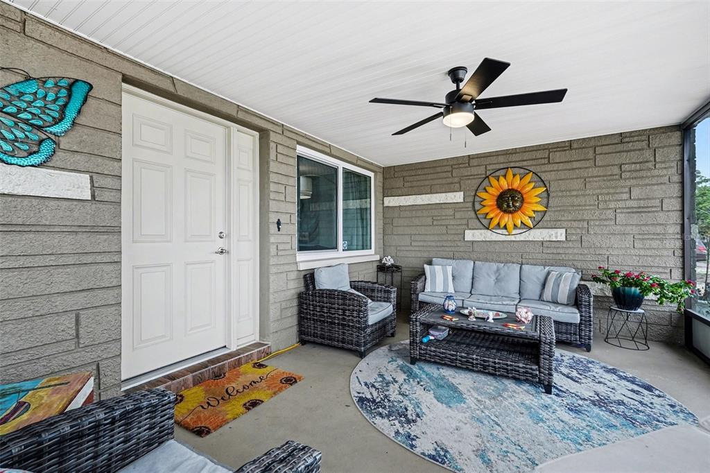A covered porch features gray stone walls, wicker furniture, a ceiling fan, and a welcome mat — 5828 1ST AVENUE, NEW PORT RICHEY, FL