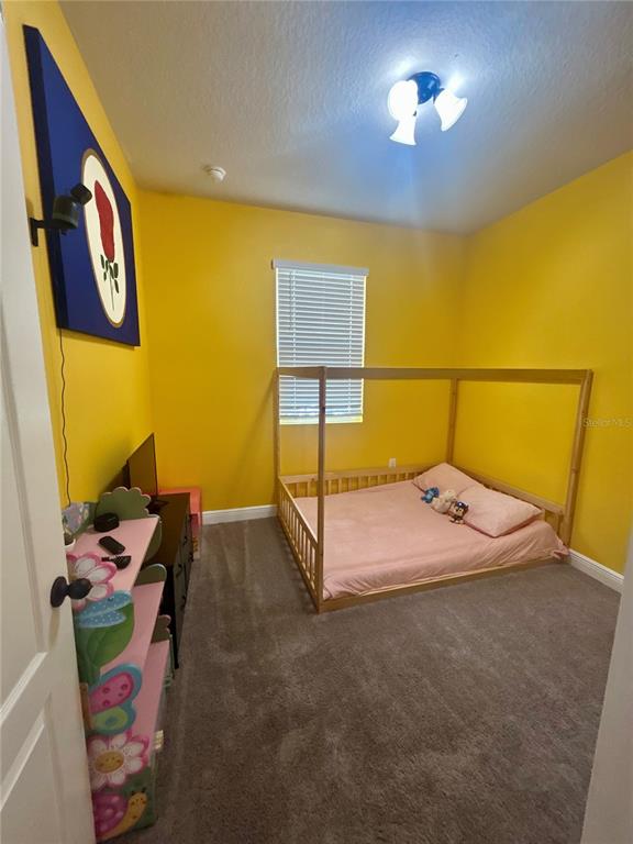A bedroom with yellow walls, gray carpet, and a wooden frame floor bed — 2587 SUMMER STAR WAY, LEESBURG, FL