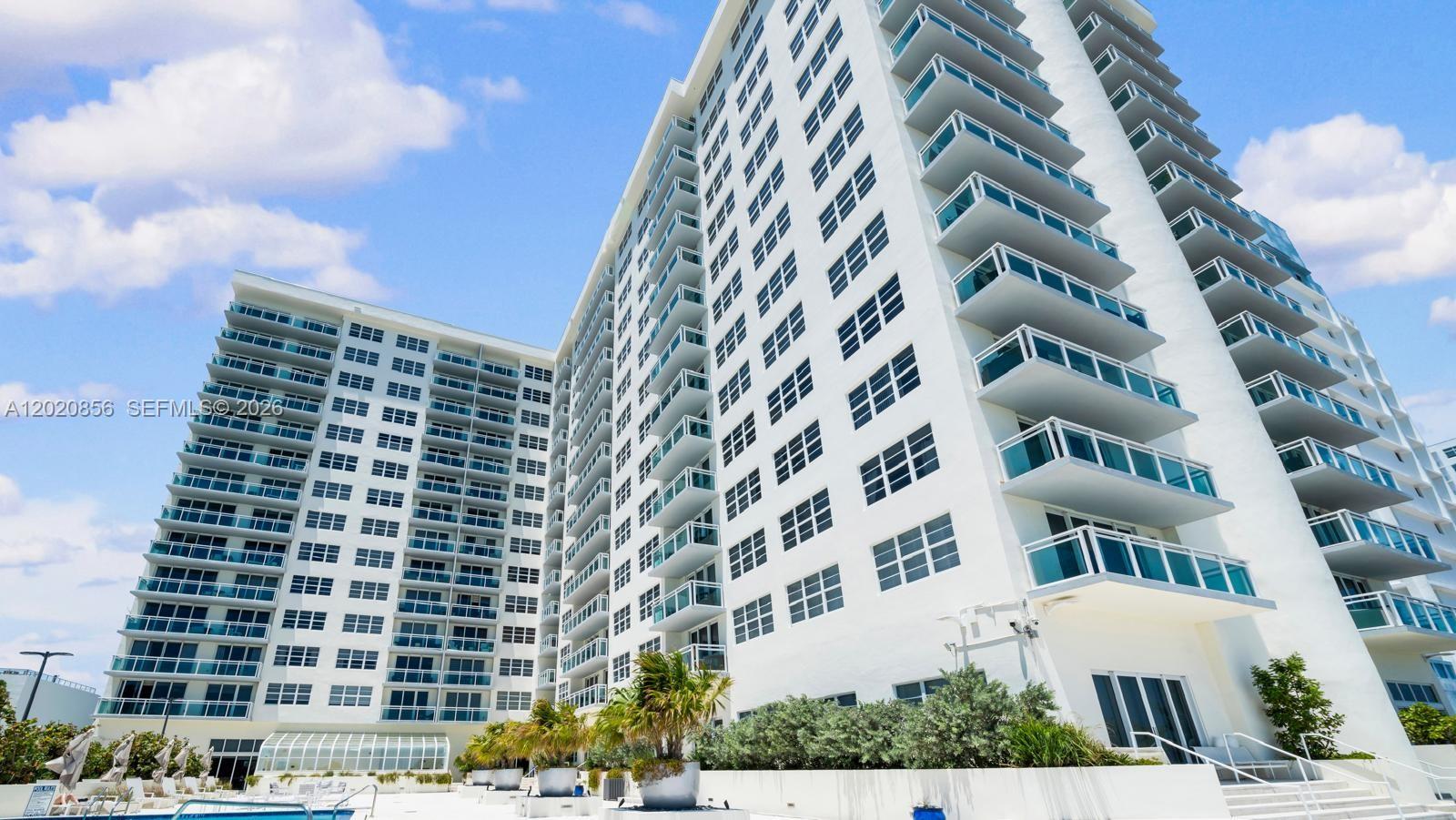 A low-angle exterior view of a tall white residential building with multiple balconies — 6917 Collins Ave # 107, Miami Beach FL 33141, MIAMI BEACH, FL